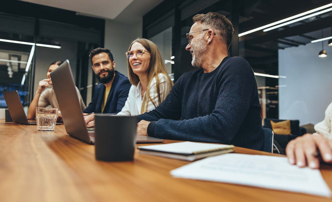 2112192335-Successful group of businesspeople having a briefing in a boardroom. Happy businesspeople smiling while working together in a modern workplace. Diverse business colleagues collaborating on a project.; Shutterstock ID 2112192335; purchase_order: QP1_5060116821; job: Anna Kayumova; client: DE04OFCX01
